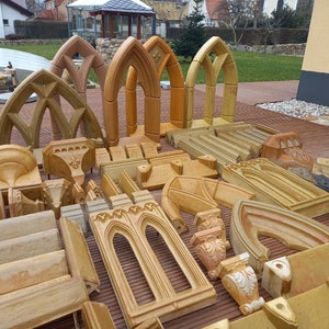 May include: A collection of tan and light brown stone architectural elements, including several pointed arch window frames, decorative corbels, carved blocks, and molded trim pieces arranged in a group on a wooden deck surface.