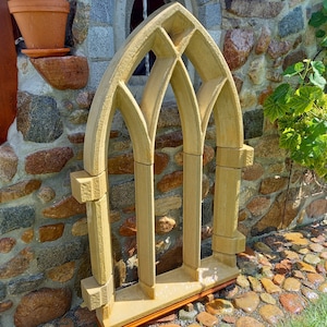 May include: A decorative stone archway with a gothic design. The archway is made of light brown stone and has three arched openings. The archway is standing in front of a stone wall.