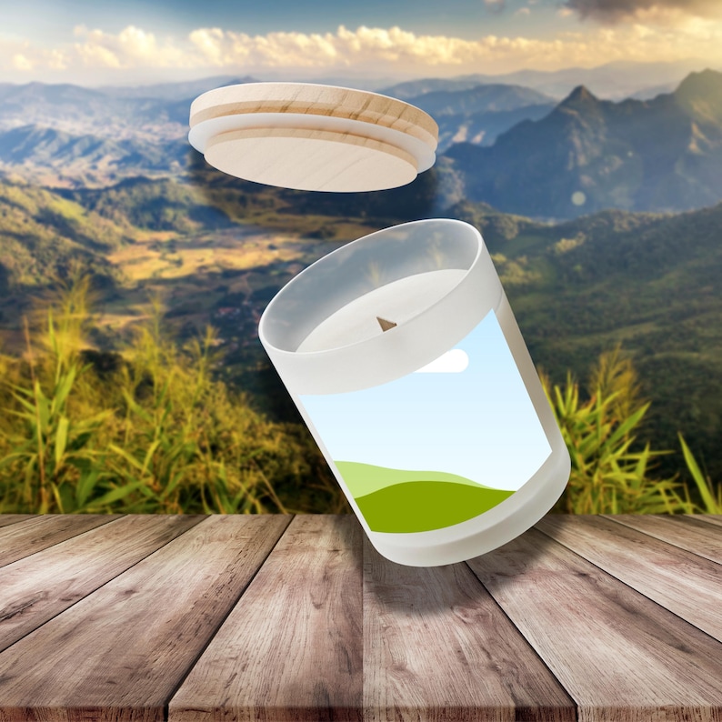Peut inclure: Une bougie en verre blanc avec un couvercle en bois, pr&eacute;sentant un paysage. La bougie est pos&eacute;e sur une surface en bois, avec des montagnes et un ciel bleu en arri&egrave;re-plan. Le couvercle est en bois clair.