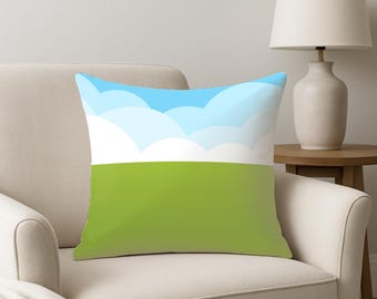 May include: Square decorative pillow with a landscape design. The top half features a blue sky with white cloud shapes, and the bottom half is a solid green. The pillow is placed on a white armchair.