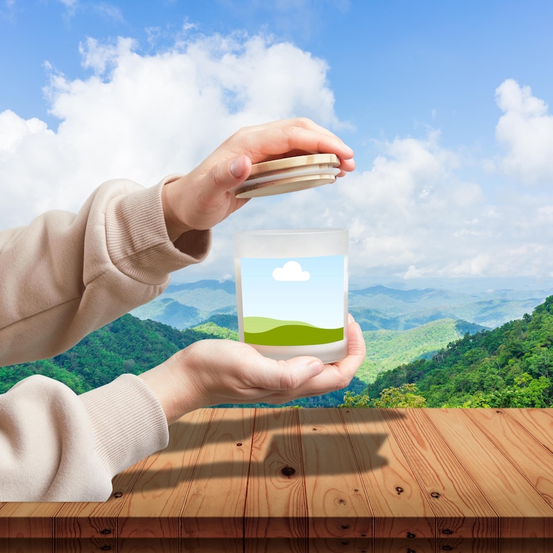Peut inclure: Un bocal en verre d&eacute;poli avec un couvercle en bois est ouvert, r&eacute;v&eacute;lant un paysage. Le bocal pr&eacute;sente un motif de ciel bleu, de nuage blanc et de collines vertes. L'arri&egrave;re-plan montre une vue panoramique sur les montagnes et le ciel bleu.