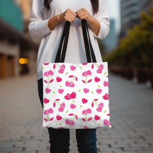 May include: A white tote bag with black handles and a pink and green cherry and heart pattern.