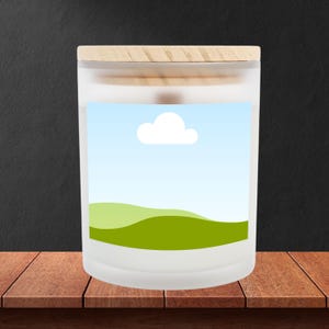 Peut inclure: Un pot de bougie en verre d&eacute;poli avec un couvercle en bois. L'&eacute;tiquette pr&eacute;sente un paysage avec des collines vertes, un ciel bleu et un nuage blanc. Le pot est pos&eacute; sur une surface en bois.