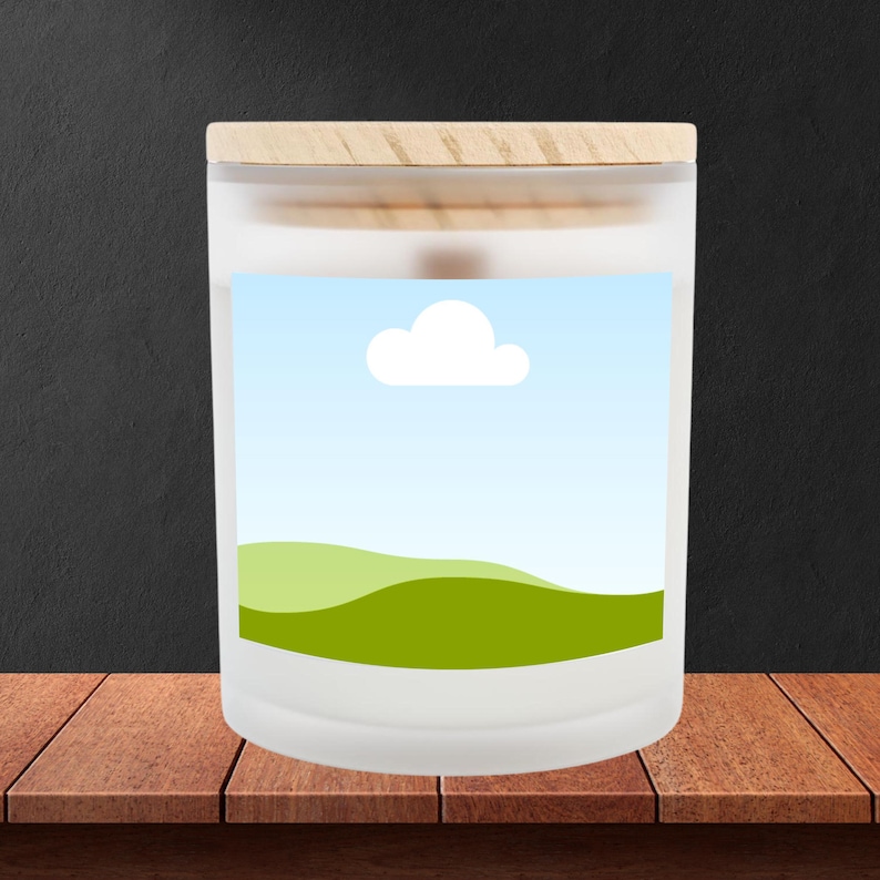 Peut inclure: Un pot de bougie en verre d&eacute;poli avec un couvercle en bois. L'&eacute;tiquette pr&eacute;sente un paysage avec des collines vertes, un ciel bleu et un nuage blanc. Le pot est pos&eacute; sur une surface en bois.