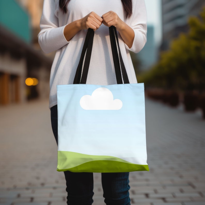 May include: A tote bag with black straps and a sky blue background. The bag has a white cloud and green hills printed on it.
