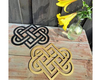 May include: Two flat, decorative trivets featuring an intricate, symmetrical Celtic knot pattern. One trivet is finished in a solid matte black, while the other is finished in a metallic gold. Both items have a cutout design with rounded edges.
