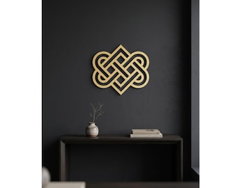 May include: A gold-colored, geometric wall art piece with an intricate knot design. The artwork is mounted on a dark gray wall. A small, decorative vase with a sprig of greenery and a stack of books are on a dark wooden console table below.