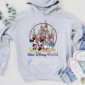 May include: A light gray hoodie featuring a colorful graphic of Disney characters, including Mickey and Minnie Mouse, Donald and Daisy Duck, and Goofy, in front of a castle. The words "Walt Disney World" are printed below the graphic.