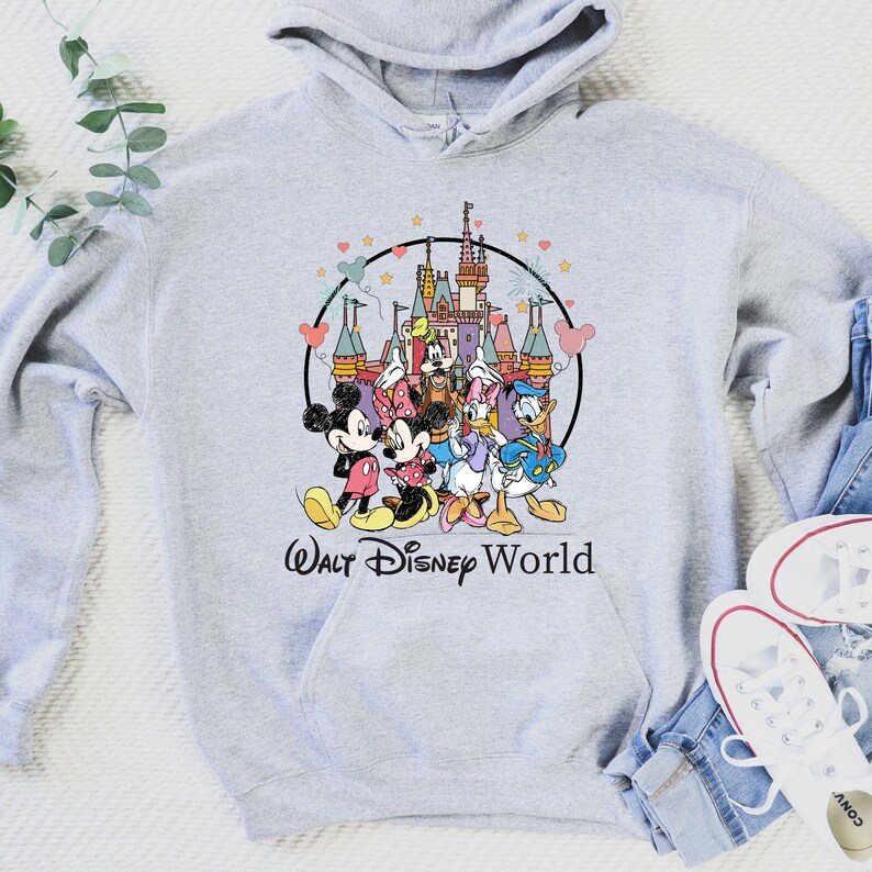 May include: A light gray hoodie featuring a colorful graphic of Disney characters, including Mickey and Minnie Mouse, Donald and Daisy Duck, and Goofy, in front of a castle. The words "Walt Disney World" are printed below the graphic.