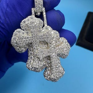 May include: A silver pendant with a floral design, covered in small, clear gemstones. The pendant has a bail for a chain. The background is a solid light blue.