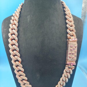 May include: Rose gold chain necklace with a large link design, encrusted with clear and pink gemstones. The necklace is displayed on a black mannequin against a blue background. The clasp features pink gemstones.