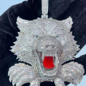 May include: A silver-toned pendant shaped like a snarling wolf head, fully encrusted with small clear stones. The wolf features a bright red enamel interior in the open mouth, two small blue stone eyes, and a rectangular bail at the top for a chain.