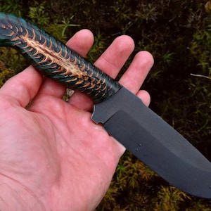 Peut inclure: Un couteau à lame noire avec un manche vert et brun. Le manche est en bois et présente un motif unique.