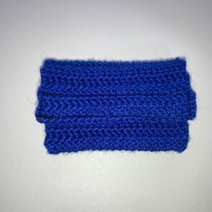 Può includere: Una piccola borsa o portafoglio in crochet blu. La borsa è realizzata con un punto semplice e ha una parte superiore ripiegata.