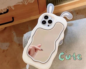 May include: White phone case with a mirror and a bunny rabbit design. The case has a cutout for the camera lens and a raised edge around the mirror. The text "Cute" is printed on the case.