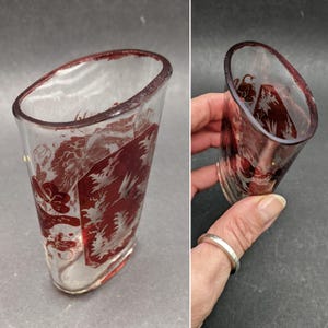 Puede incluir: Una taza de vidrio transparente con un diseño rojo grabado de un árbol y un pájaro. La taza tiene forma ovalada y tiene un fondo redondeado.