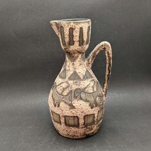 May include: A textured, tan ceramic jug with a handle and spout. The jug features dark brown geometric and animal designs. The overall design is rustic and vintage, suitable for decorative use.