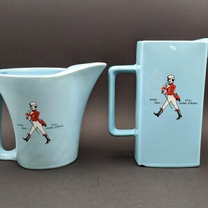 K&ouml;nnte beinhalten: Zwei blaue Keramikkr&uuml;ge mit einer Grafik eines laufenden Mannes und dem Text "Born 1820 - Still Going Strong".