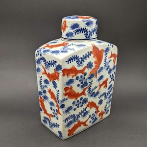 May include: A rectangular ceramic jar with a removable lid, featuring a white base decorated with a repeating pattern of orange koi fish and blue aquatic plants. The design covers all visible sides of the jar and the top of the lid.