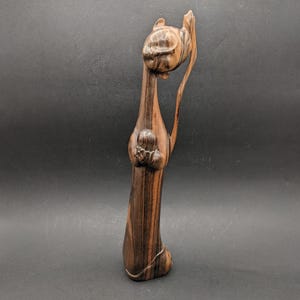 Puede incluir: Una escultura de madera de un gato de pie sobre sus patas traseras con las patas delanteras levantadas. El gato está tallado en madera oscura con vetas marrón claro. La escultura mide aproximadamente 30 cm de alto.