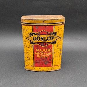 Può includere: Scatola di latta vintage Dunlop "Major Patch Strip Outfit". Il contenitore rettangolare ha uno sfondo giallo con accenti rossi e testo nero. Il testo include "Dunlop" a forma di diamante e "Major Patch Strip Outfit".