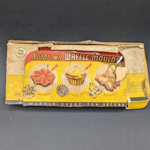 May include: Vintage Nutbrown Waffle Moulds box. The yellow and red box features illustrations of waffle shapes: rosette, patty shell, and butterfly. Text reads "A Waffle Every Ten Second". The box is aged with wear.