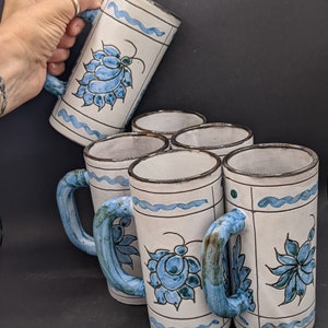 Peut inclure: Ensemble de cinq mugs en céramique avec des motifs floraux bleus et blancs. Les mugs ont des bords et des poignées marrons.