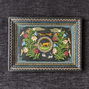 May include: Black rectangular tray with a vibrant floral and animal design. The tray showcases a central circular image of a deer, surrounded by flowers, birds, and small animals. The border has a decorative zigzag pattern.
