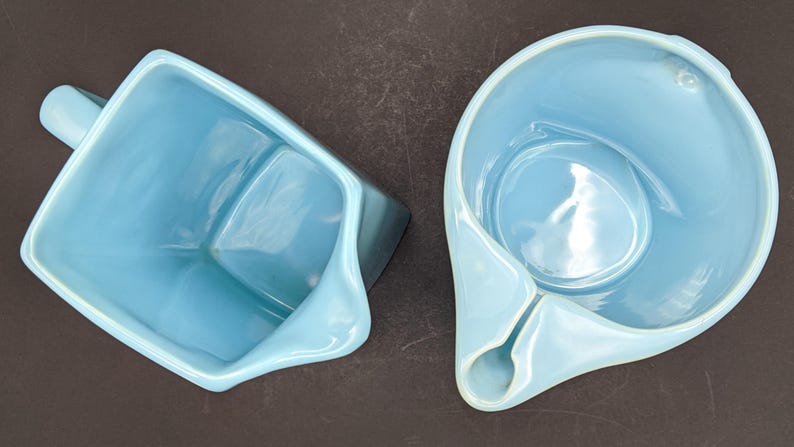 K&ouml;nnte beinhalten: Zwei hellblaue Keramikkr&uuml;ge, einer mit quadratischem Boden und Henkel, der andere mit abgerundetem Boden und Ausguss.