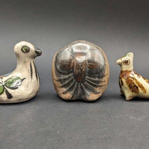 May include: Three ceramic bird figurines in a row. The first is a white bird with black stripes and floral accents. The second is a brown, egg-shaped bird. The third is a bird with brown and tan spots.