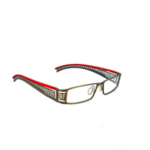 Puede incluir: Un par de gafas de metal marrón con detalles rojos en las patillas. Las gafas tienen una montura rectangular y lentes transparentes.