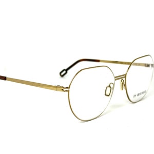 May include: Gold-tone metal eyeglasses with a rounded, octagonal frame and clear lenses.
