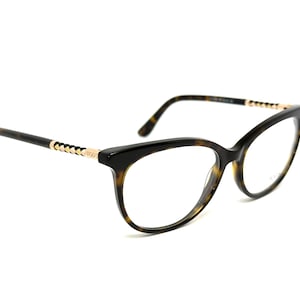 Puede incluir: Gafas de vista de carey con un acento dorado en las patillas. Las gafas tienen una forma de ojo de gato y lentes transparentes.