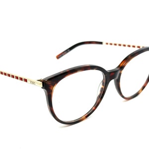 May include: Tortoise shell eyeglasses with a gold metal frame and red accents. The glasses have a cat-eye shape and clear lenses.