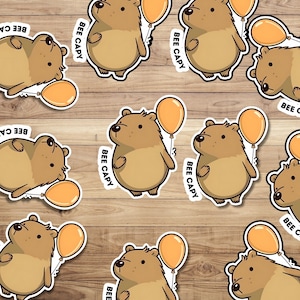May include: A set of 10 brown bear stickers with orange balloons. Each sticker has the text "BEE CAPY" on it.