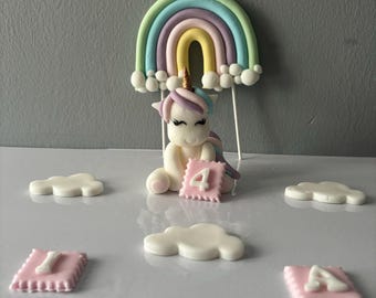May include: A unicorn cake topper with a rainbow, clouds, and the name "Isla" and the number "4" in pink and white.