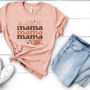 May include: A peach-colored t-shirt with the text "football mama mama mama" and a brown football graphic.