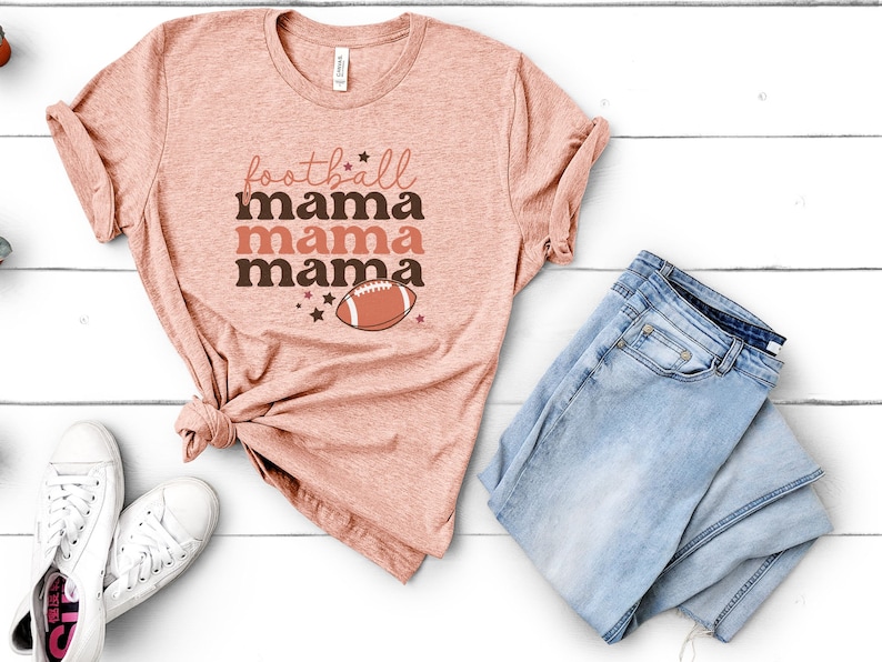 May include: A peach-colored t-shirt with the text "football mama mama mama" and a brown football graphic.