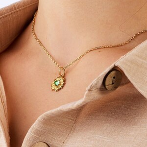 Puede incluir: Un collar de cadena dorada con un peque&ntilde;o colgante de piedra preciosa verde en forma de sol.