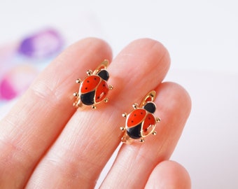 May include: A pair of gold-toned ladybug earrings with red and black enamel. The earrings are small and delicate, perfect for a child.