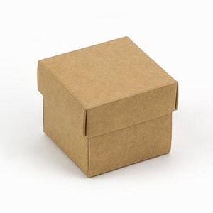 Puede incluir: Una pequeña caja cuadrada de cartón marrón con tapa. La caja está hecha de cartón liso, sin imprimir, y se encuentra sobre una superficie blanca. La tapa encaja perfectamente sobre la base, creando un diseño limpio y sencillo.