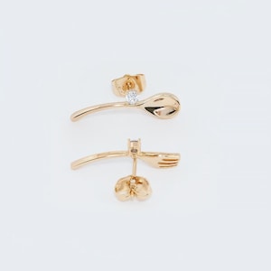 May include: A pair of gold earrings with a spoon and fork design. Each earring features a small clear stone.
