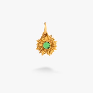Puede incluir: Un amuleto de girasol dorado con una piedra preciosa verde en el centro.