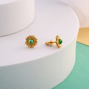 Puede incluir: Un par de pendientes de oro con una piedra preciosa verde en el centro de cada pendiente. Los pendientes tienen forma de girasol.