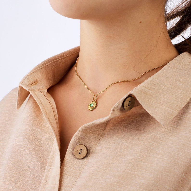 Puede incluir: Un collar de cadena dorada con un peque&ntilde;o colgante de piedra preciosa verde en forma de sol.