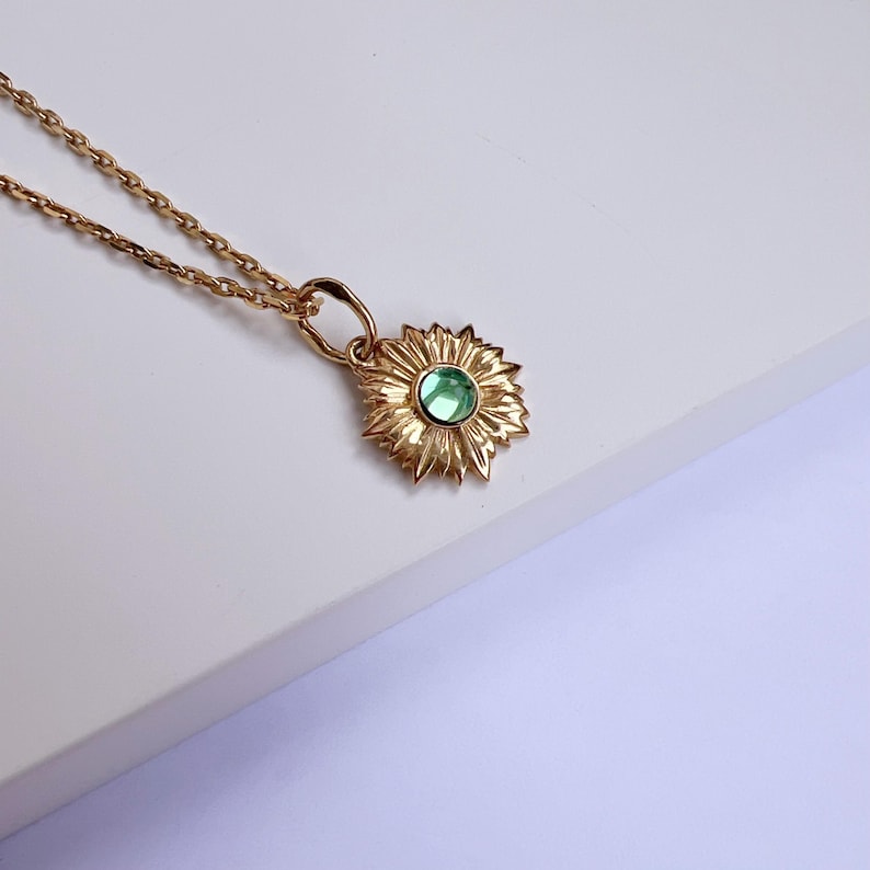 Puede incluir: Un collar de oro con un colgante de girasol con una piedra preciosa verde en el centro.