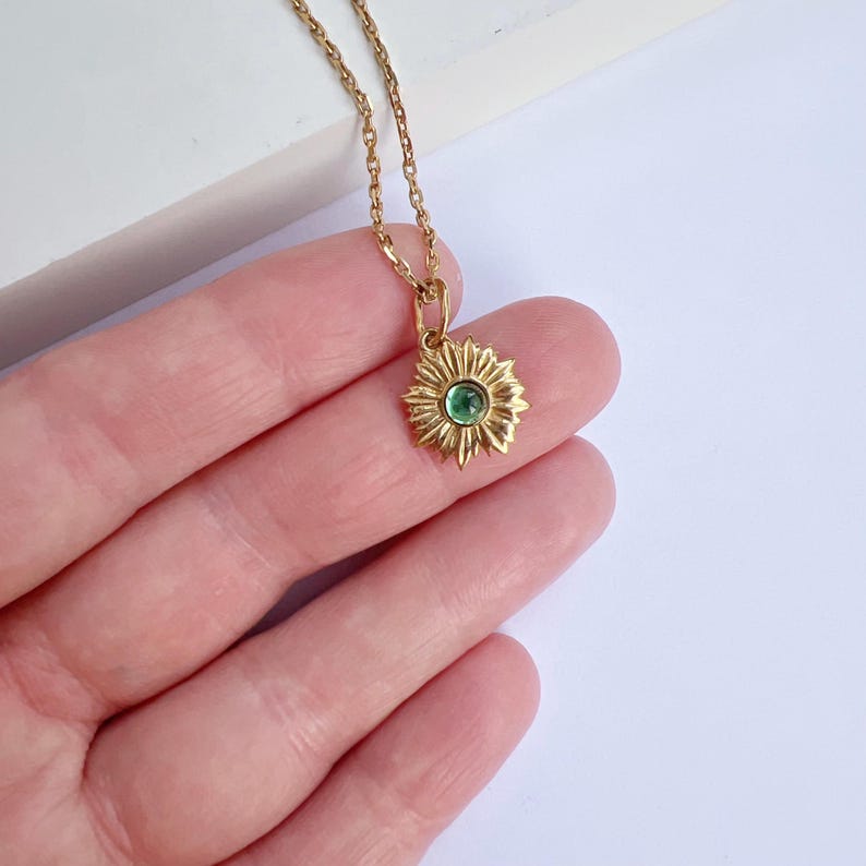 Puede incluir: Un collar de oro con un colgante de girasol con una piedra preciosa verde en el centro.