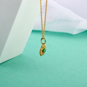 Puede incluir: Un collar de cadena dorada con un colgante que presenta un amuleto de ojo turco verde. El colgante tiene forma de sol con un dise&ntilde;o detallado.