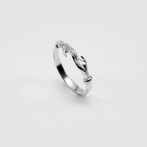 May include: A silver ring featuring a design of two hands clasped together. The ring has a smooth, polished finish and a minimalist style. The hands are intricately detailed, creating a unique and symbolic piece of jewelry.
