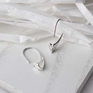 May include: A pair of silver earrings with a unique geometric design. The earrings are shaped like a curved arrow with a pointed tip.